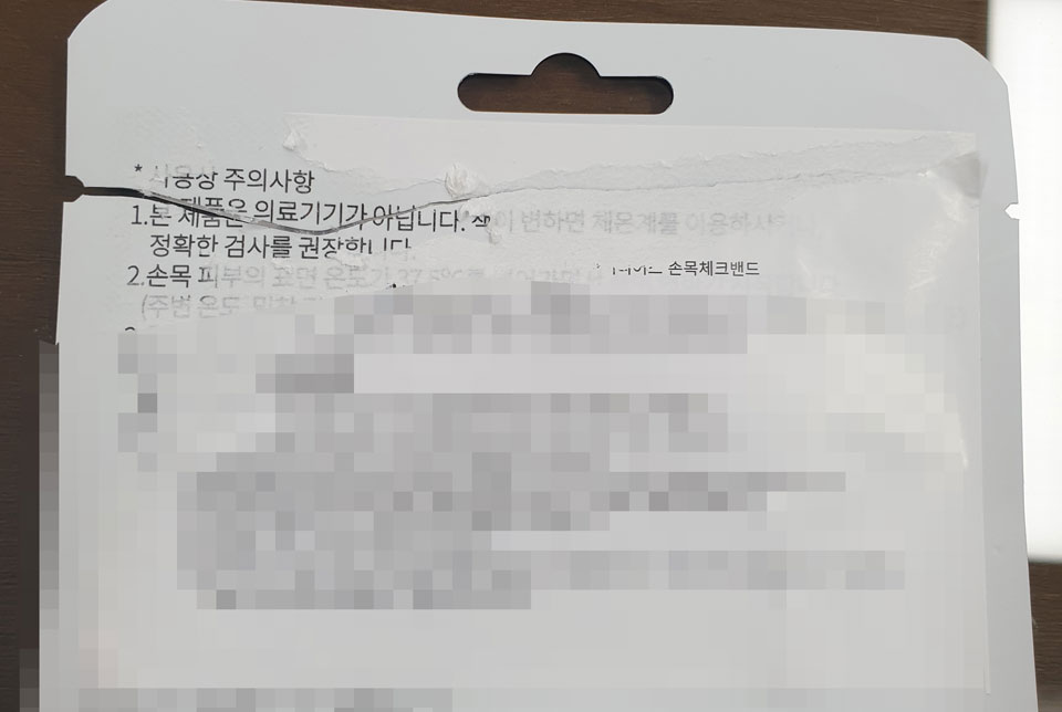 ▲납품된 체크밴드 뒷쪽에 덧붙인 스티커를 제거하자 의료기기가 아니라는 문구가 나와 의혹을 사고 있다.